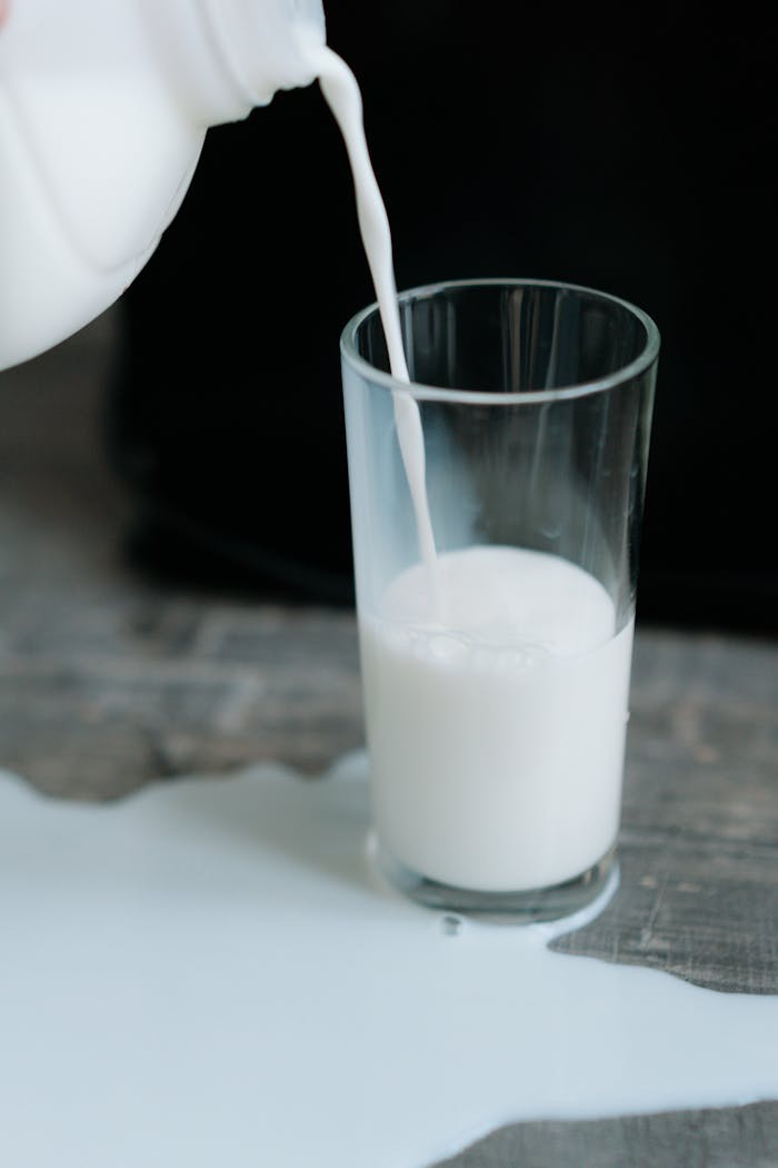 Close-up of milk being poured into glass with spilled milk on wooden table.